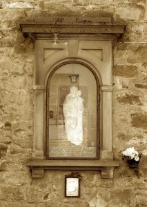 White Virgin Mary sculpture behind glassed in case of monument built into wall.