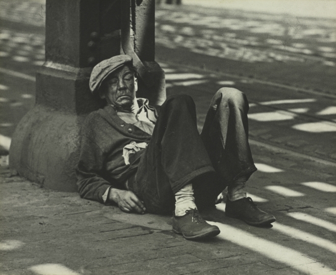 Man sleeps on sidewalk leaning against cement pillar