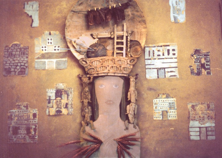 female figure with hands cholding wheat and elaborate headdress containing yarn, needles, and other items, with several additional clothes on line, surrounded by 10 full or partial house facades.