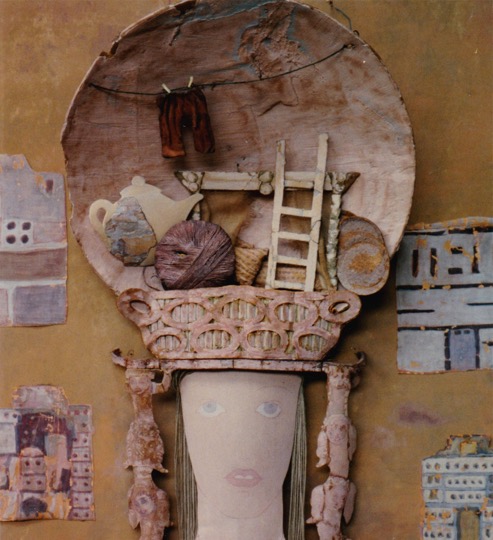 Female head with headdress containing ball of yarn, teapot, ladder, plates, pillows, and a clothesline with pair of pants 
