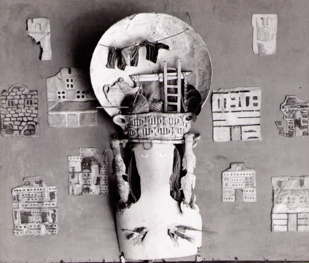 multimedia assemblage of female heaad with headdress composed of domestic items and architectural forms.