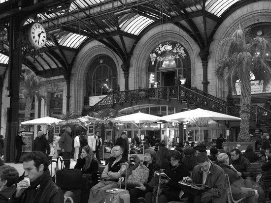 interior of Gare de Lyon, with people waiting on benches in front of a restaurant with umbrellas over tables.